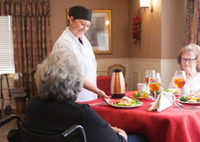 A woman chef serving food to two woman at a table